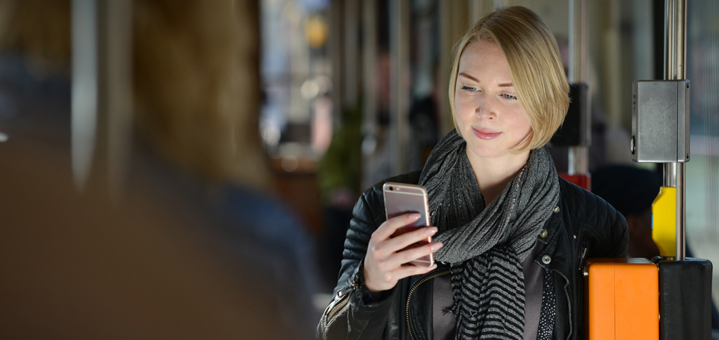 Eine Frau steht in einer DVG-Bahn und schaut in ihr Smartphone