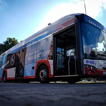 Seitenansicht eines modernen DVG-Wasserstoffbusses auf grauem Hintergrund.