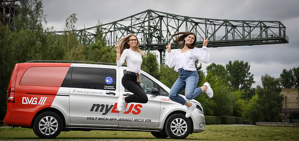 Zwei junge Frauen springen vor einem myBUS-Fahrzeug im Landschaftspark Nord in die Höhe