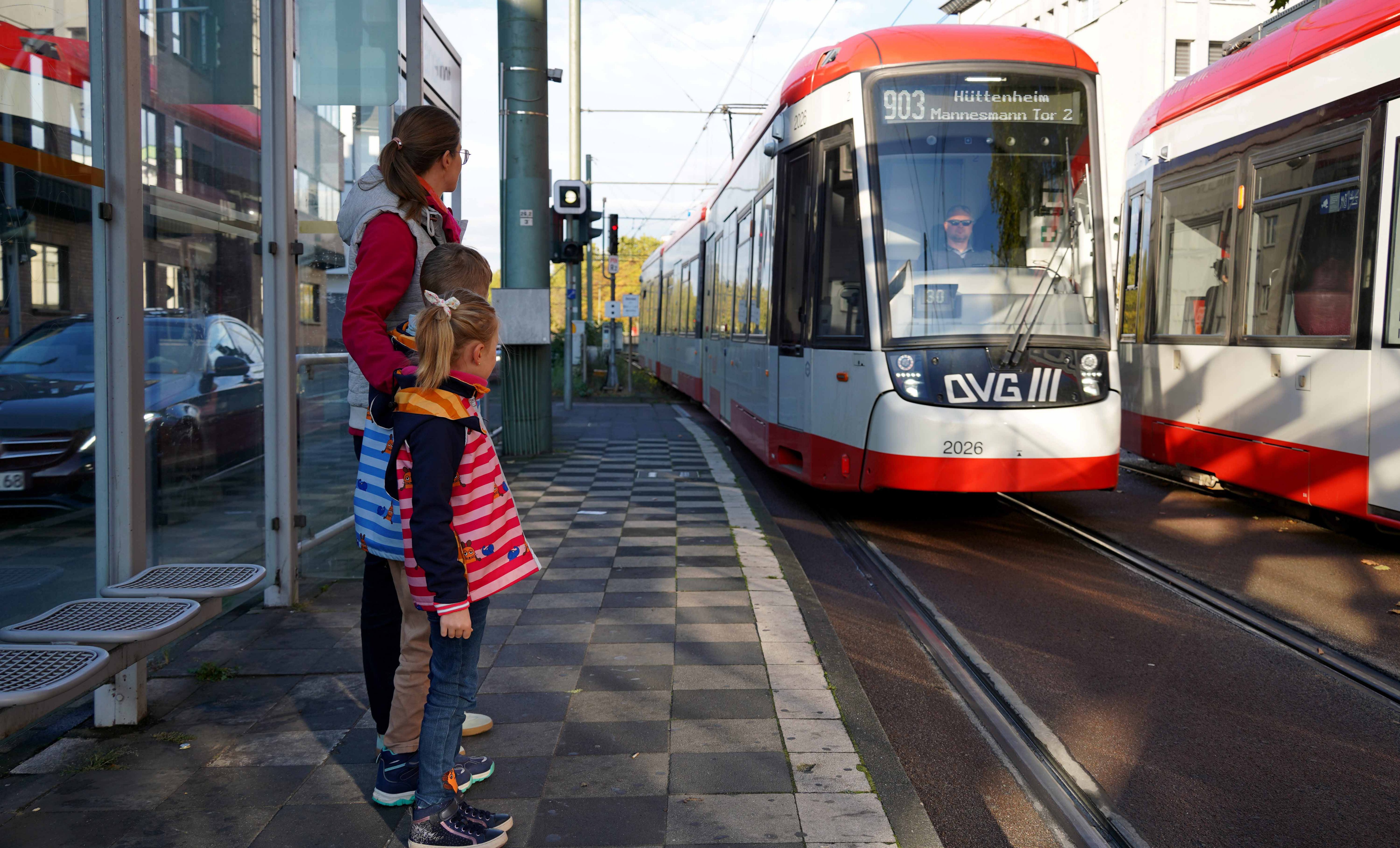Eine Mutter wartet mit ihren zwei Kindern auf die Bahn, die gerade einfährt.
